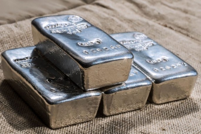 Four silver bars are stacked on a beige textured fabric surface. The bars display engraved text and numeric values, including '999' and '0.25 kg'. The setting emphasizes the metallic sheen and industrial quality of the silver. The image conveys a sense of value and material wealth.